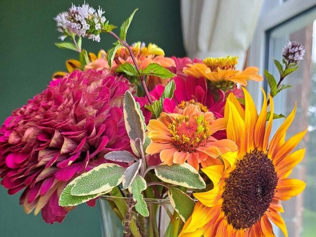 A summer flower arrangement with a mix of flowers and herbs in a clear vase.