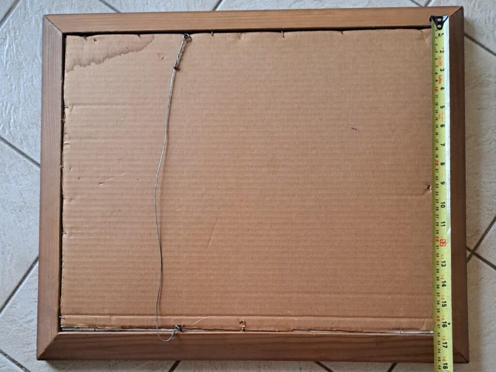 Measure the back of a wooden picture frame with a measuring tape.