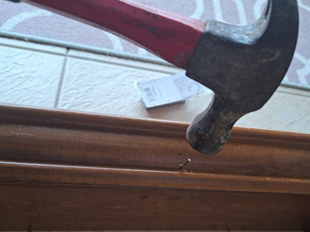 Hammering in a finishing nail to attach a wooden picture frame to a wooden box to grow herbs indoors.