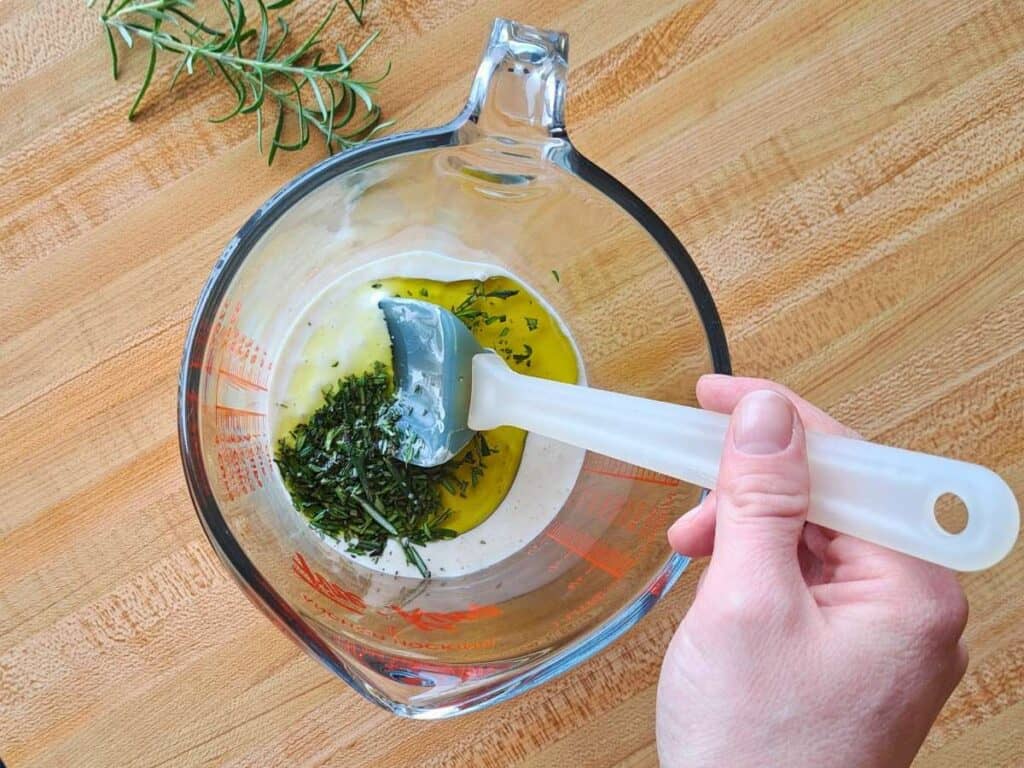 Mixing the homemade rosemary cracker recipe up in a glass measuring cup with a rubber spatula.
