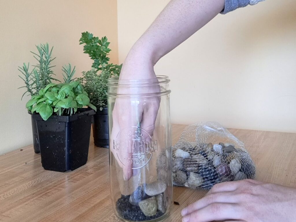 Placing rocks in the mason jar as the second layer.