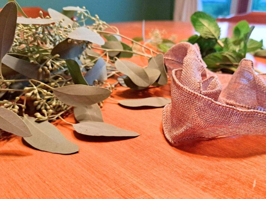 Eucalyptus, mint, sage, and burlap ribbon sitting on a wooden table.