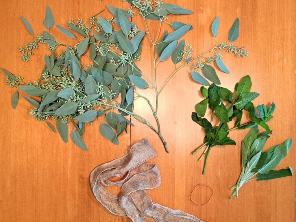 Herbs, ribbon, and an elastic band gathered and sitting on a wooden table.
