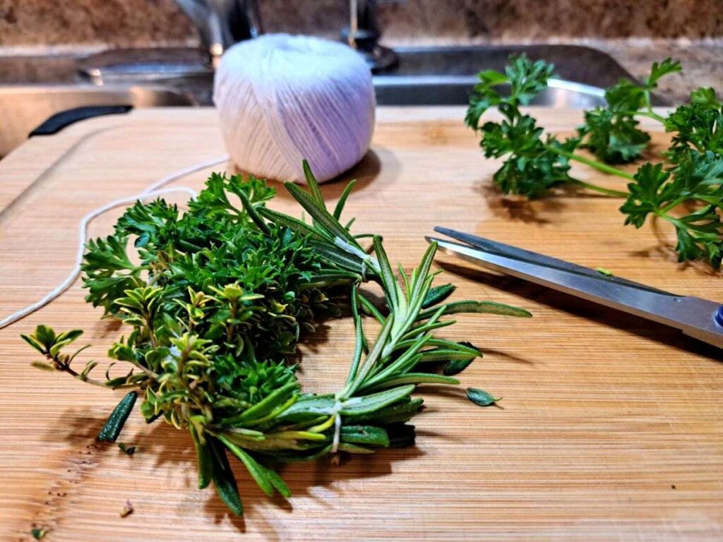 A completed herbal soup wreath laying on the cutting board with some other supplies around it.