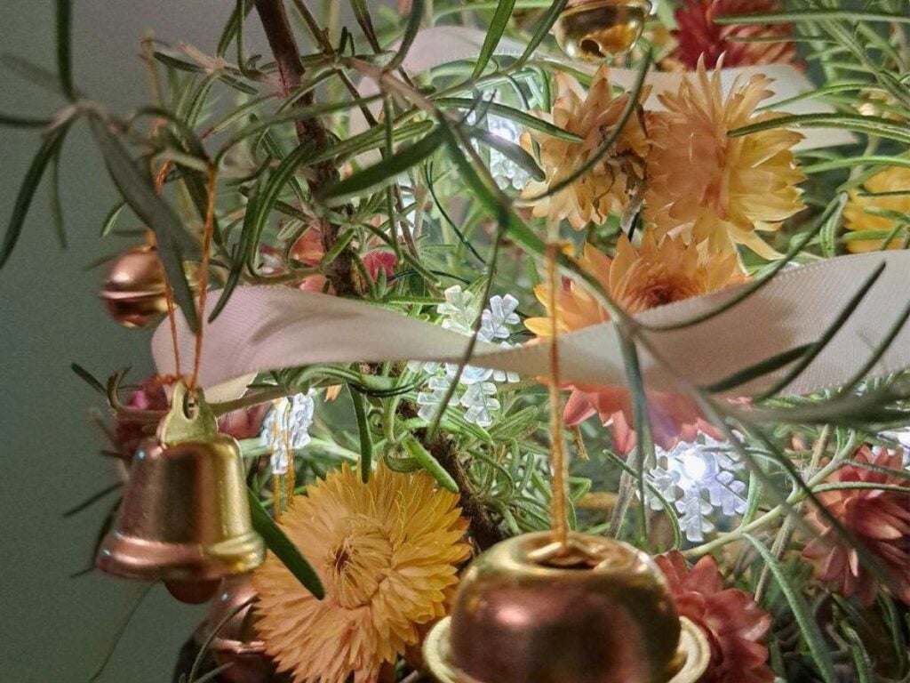 Close up of metal bells and dried strawflowers on a mini rosemary tree.