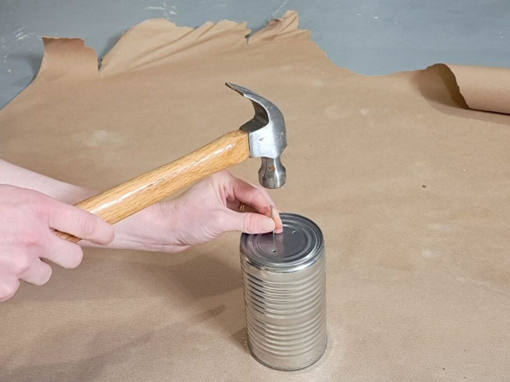 Someone hammering a small nail into the bottom of a metal tin can.