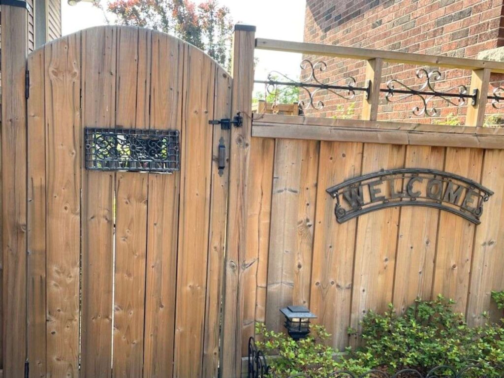 An image of a wooden garden gate with metal details including a welcome sign.