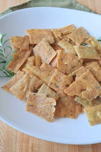 Rosemary olive oil sourdough crackers laying on a white plate on a wooden counter.