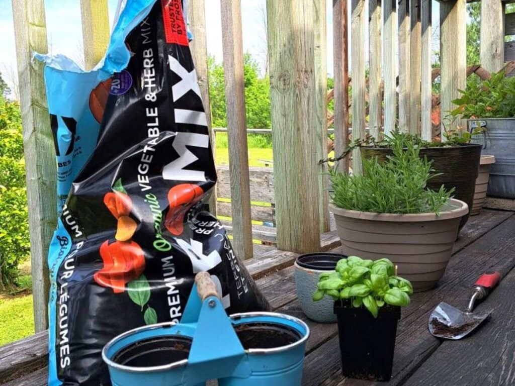 Potting mix, a shovel, pots, and herbs ready to be planted.