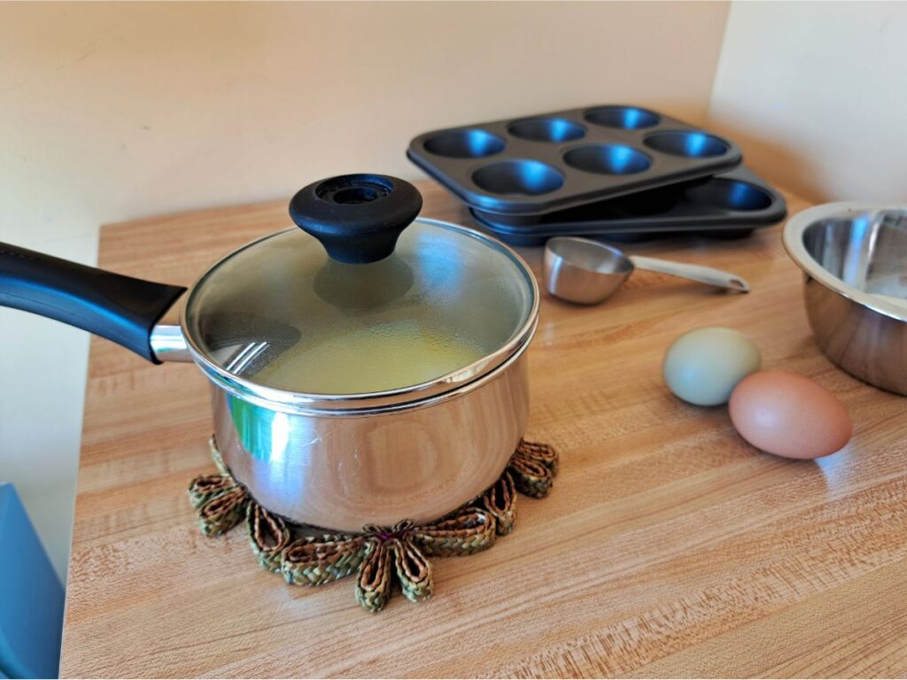 A small saucepan sitting on the counter with muffin tins behind it.