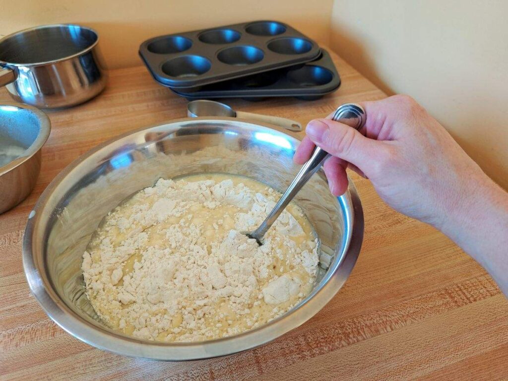 A hand stirring the wet and dry ingredients together in a metal bowl.