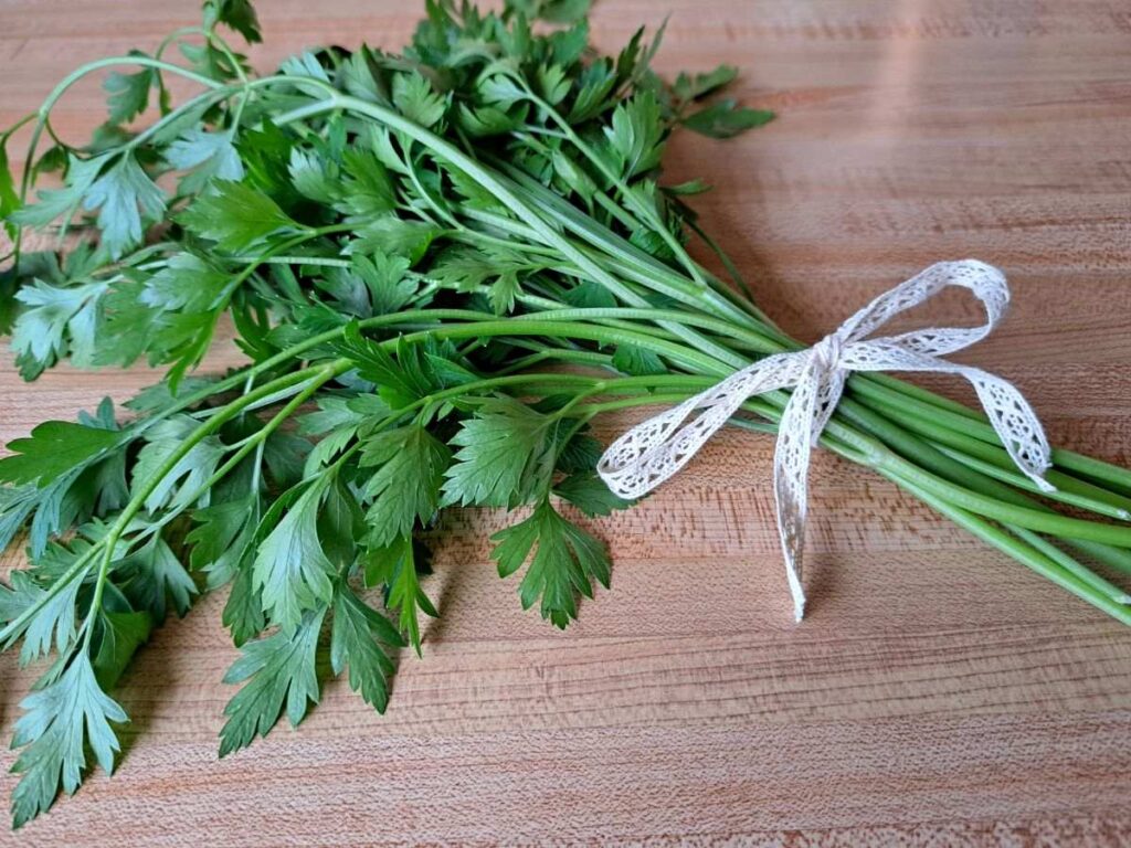A bunch of parsley on a wooden counter tied with a lace ribbon.