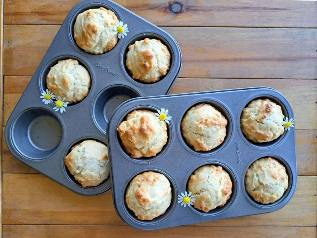 Golden brown chamomile and honey sourdough discard muffins sitting in metal muffin tins on a wooden table.