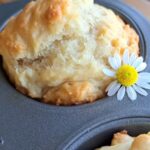 A close up of a honey chamomile muffin in a muffin tin with a chamomile flower on it.