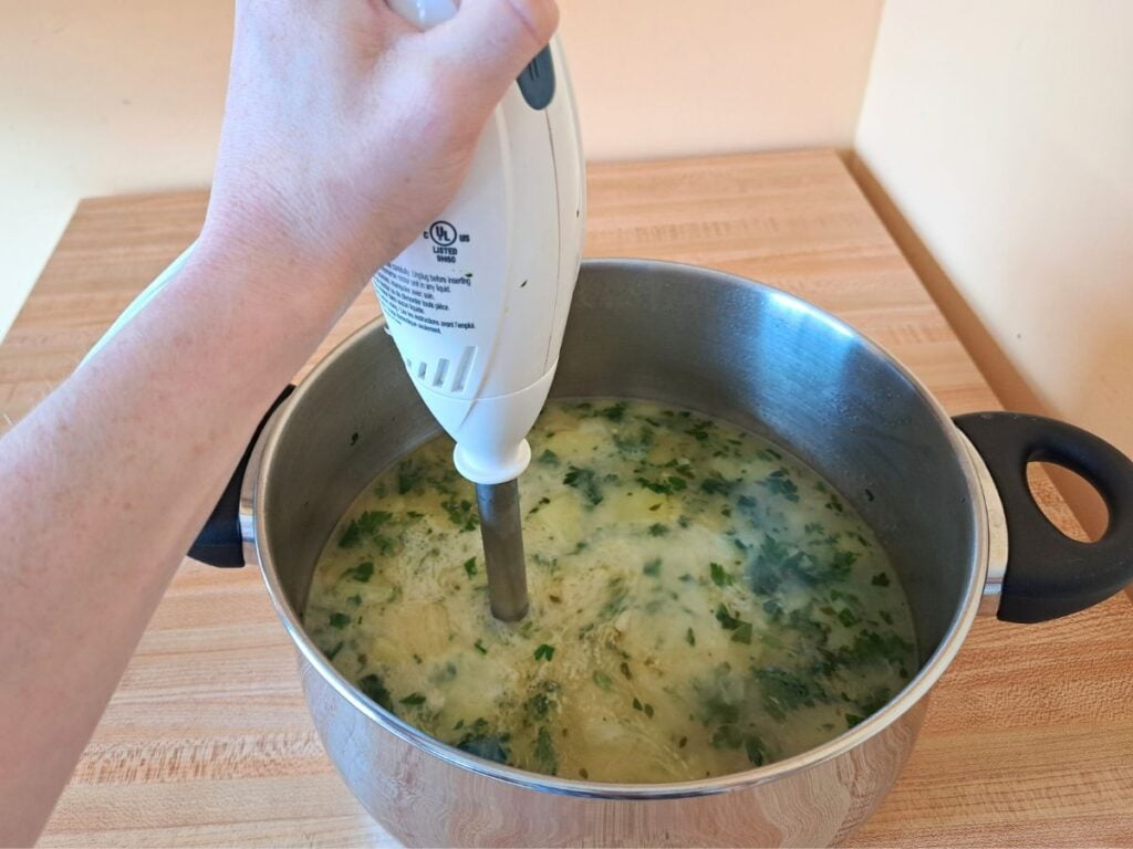 Using an immersion blender to puree the cream of potato and parsley soup.