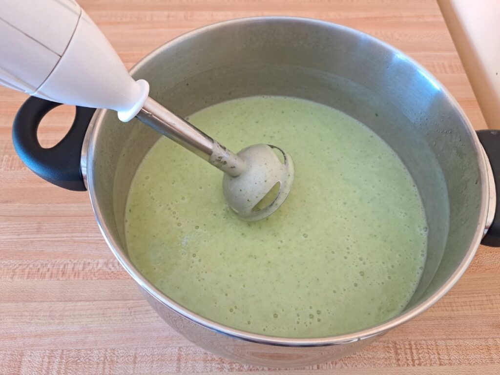 A close up showing the pureed soup in a metal pot with the immersion blender held over it.