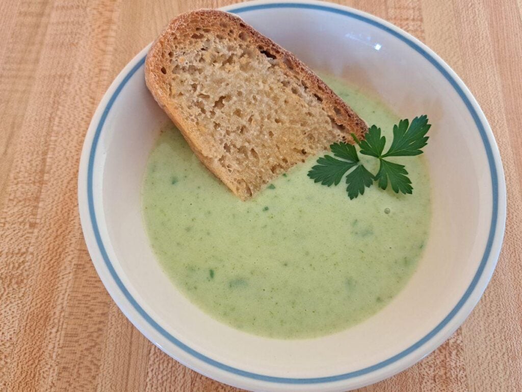 A close up of creamy potato soup with parsley in it and a piece of toast and butter.