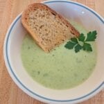 A close up of creamy potato soup with parsley in it and a piece of toast and butter.