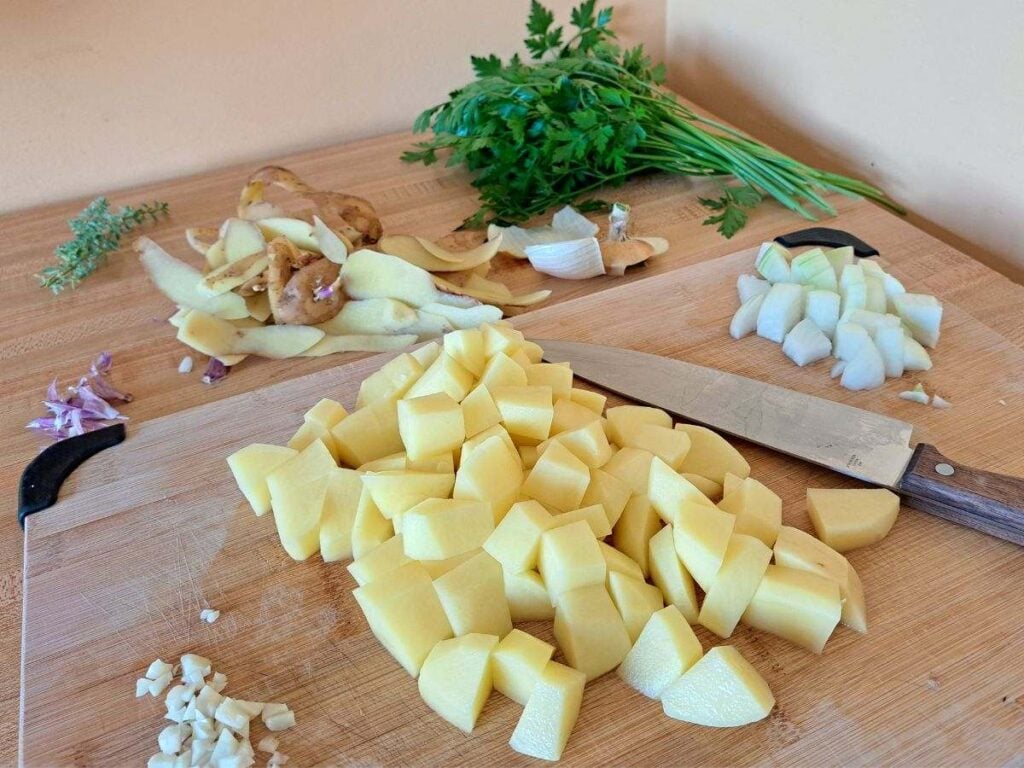 A cutting board with potatoes, onion, and garlic being chopped up.