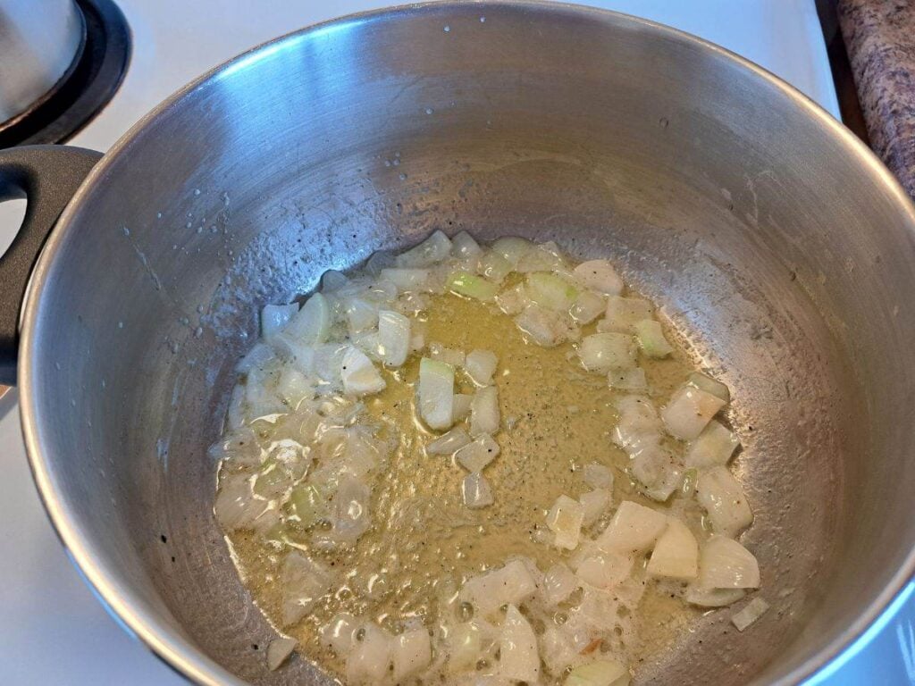 Melting butter in a pot on the stove and sauteing onions.