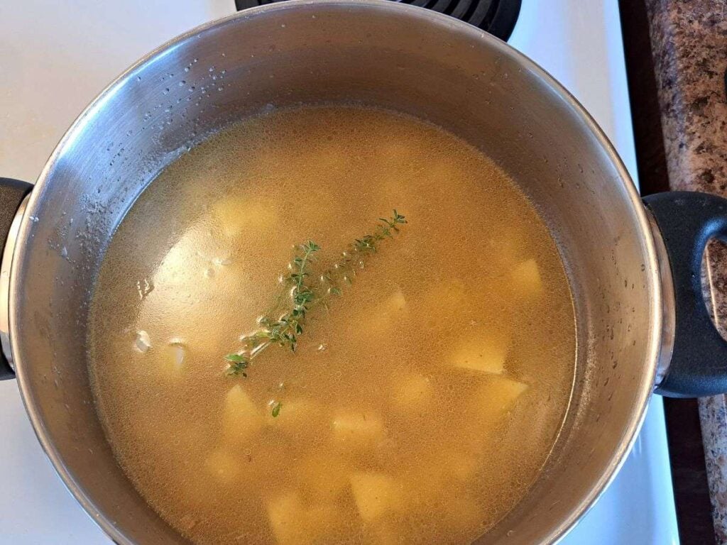 Chicken broth, potatoes and thyme in a pot on the stove.