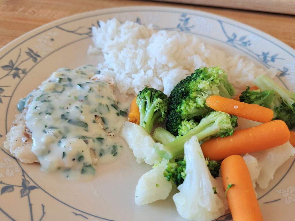 A close up of fish in parsley sauce served on a dinner plate.