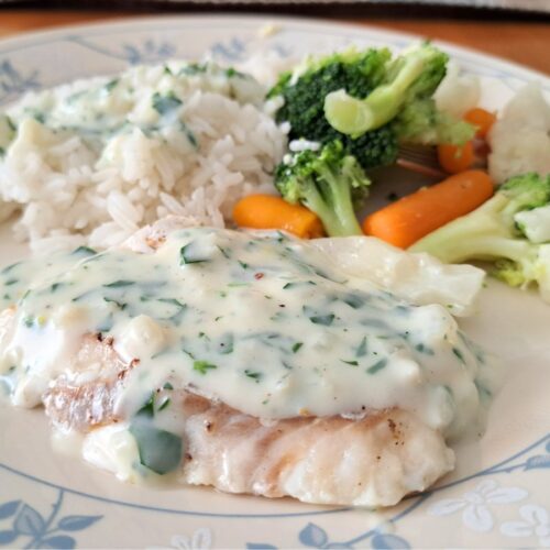 A dinner plate with white fish in parsley sauce, rice, and mixed vegetables.