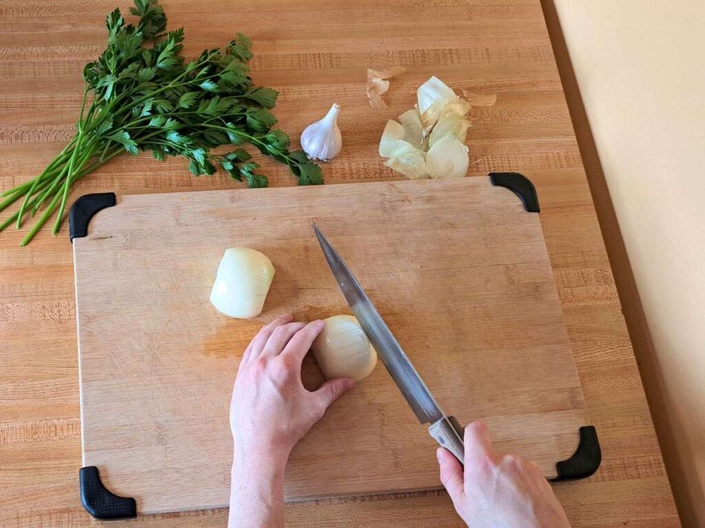 Chopping onions on a wooden cutting board, with parsley and garlic in the background.