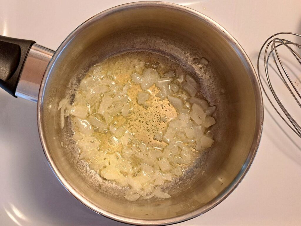 Sauteing onions in melted butter in a metal saucepan on the stove.
