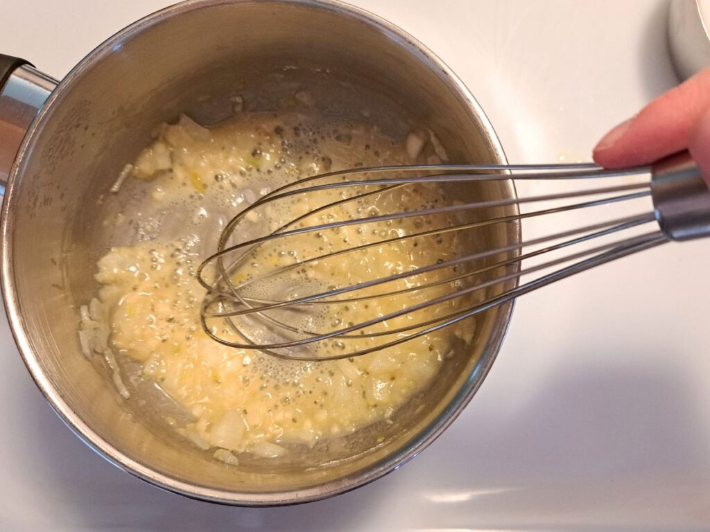 Mixing flour in melted butter in a saucepan on the stove to make a roux.