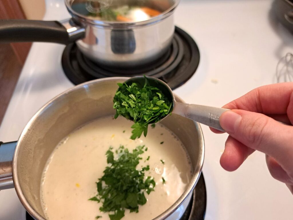 Adding parsley to the thickened white sauce on the stovetop.