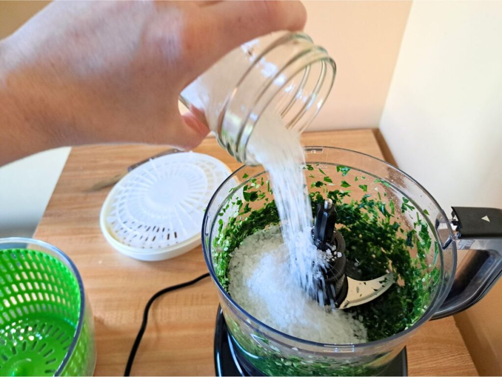 Adding coarse sea salt into the food processor with the garlic and parsley.