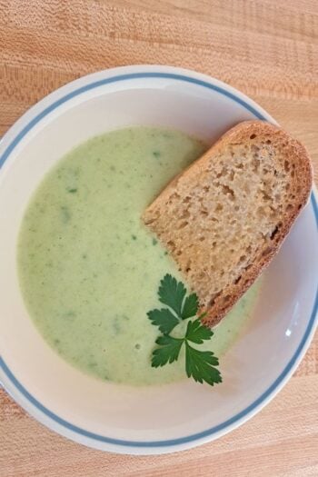 A close up of parsley soup in a bowl with a piece of toast.
