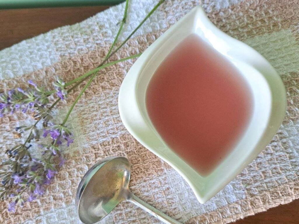 A close up of lavender simple syrup with honey in a white dish with a spoon and sprigs of lavender.