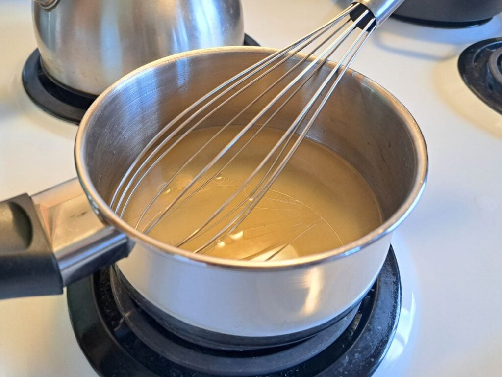 Whisking water, honey, and sugar in a saucepan on the stovetop.