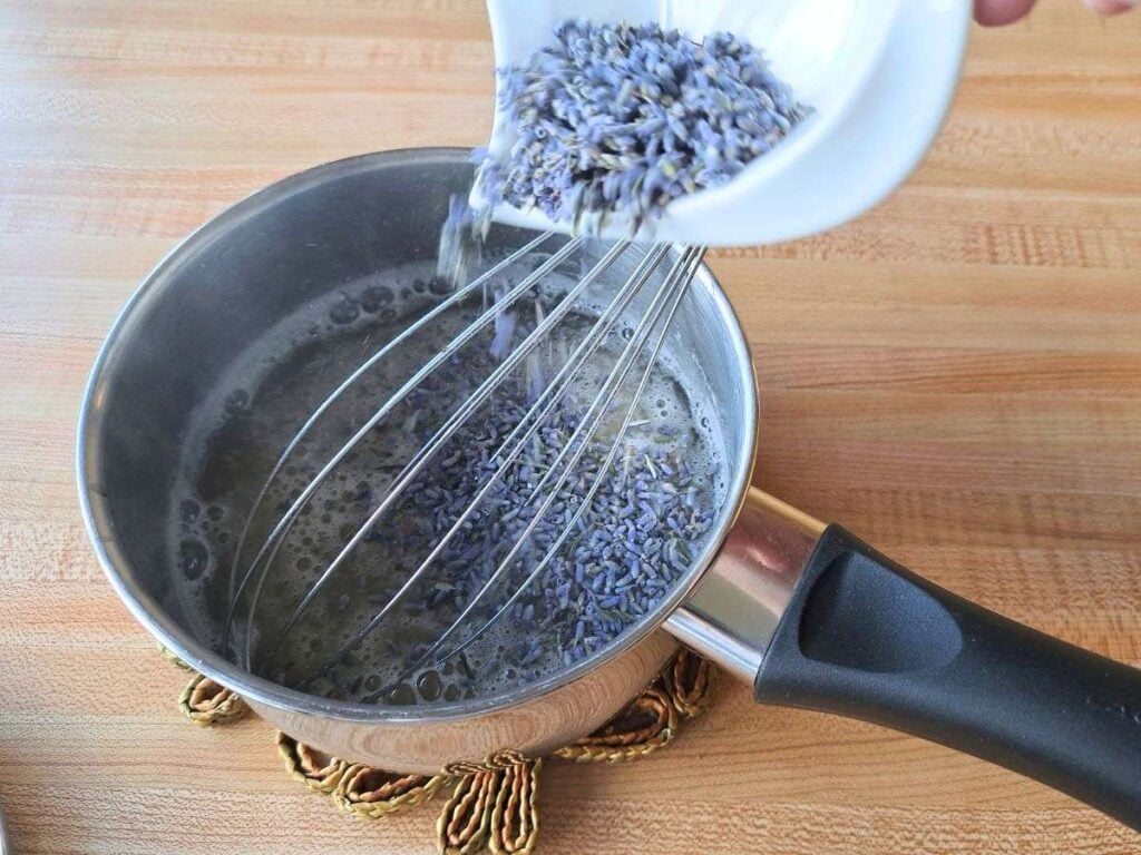 Adding dried culinary lavender buds to a metal saucepan.