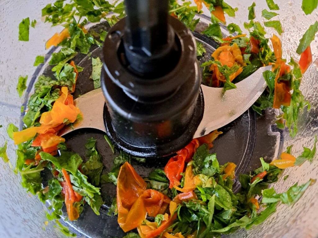 A close up of tomatoes and basil chopped up in a food processor bowl.