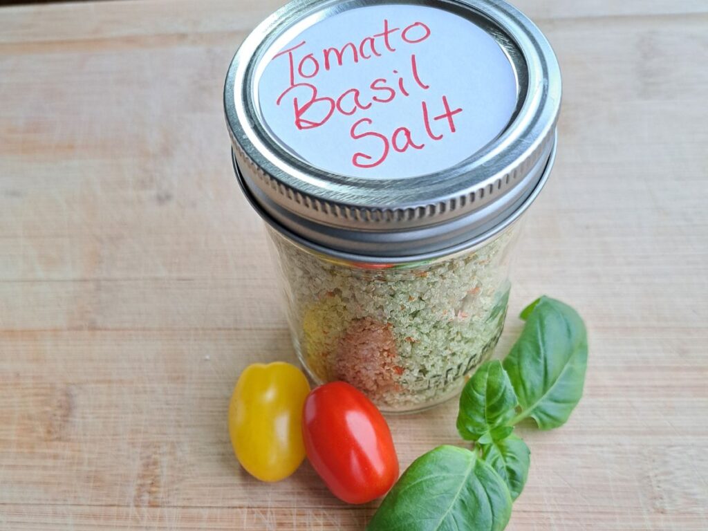 Tomato Basil infused salt in a canning jar with some tomatoes and basil sitting beside it.