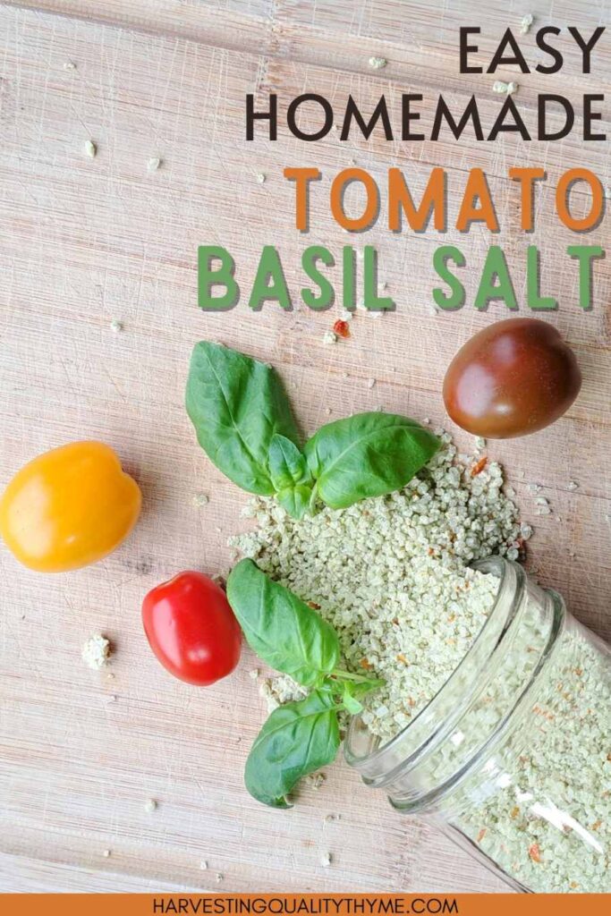 Herb infused sea salt spilling out of a canning jar on to a wooden cutting board. There are also basil leaves and tomatoes scattered around.
