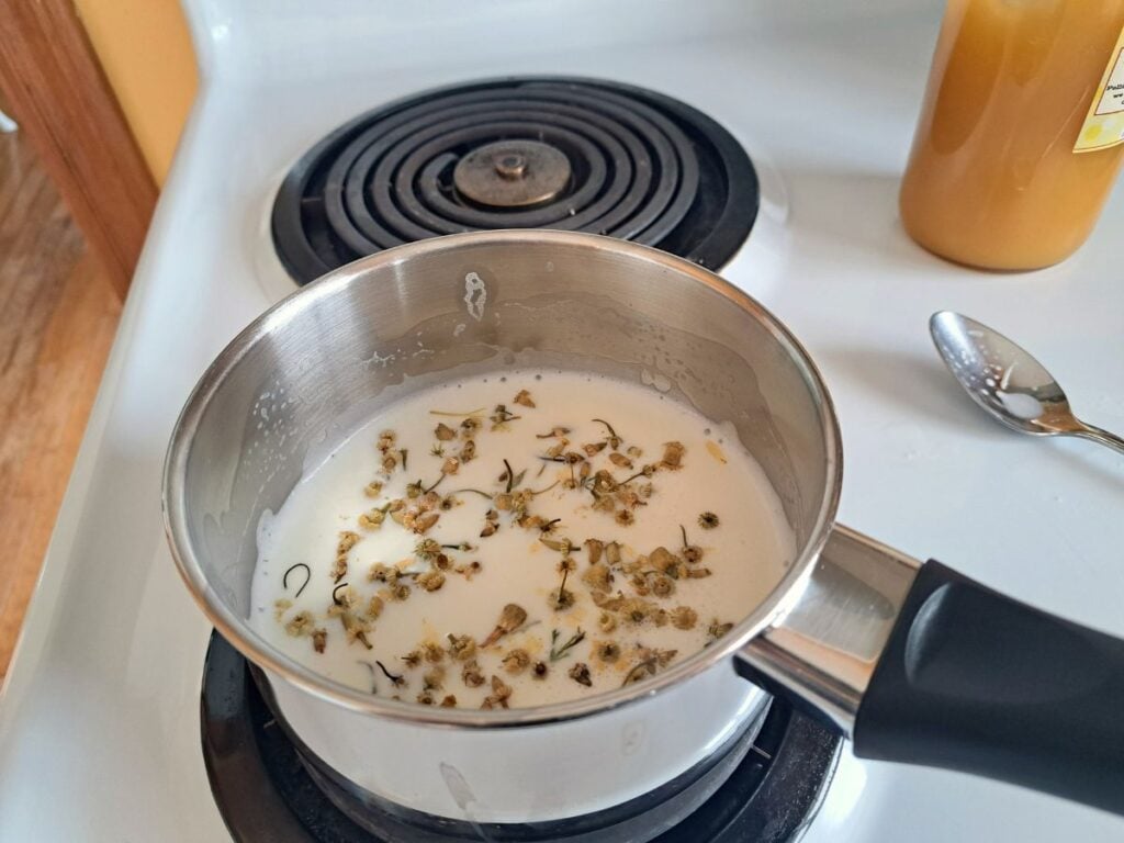 Dried chamomile steeping in milk in a saucepan on the stovetop.