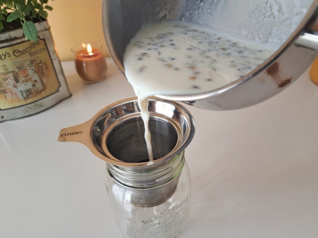 Straining chamomile out of the milk into a mason jar.