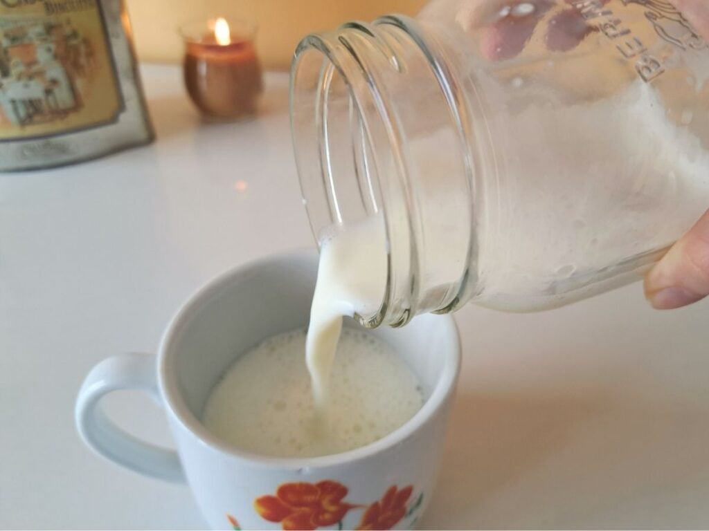 Pouring frothed milk from a mason jar into a mug.
