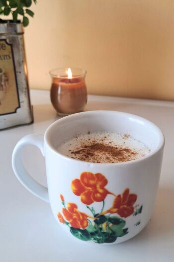 A warm nighttime drink sitting on a counter with a candle in the background.