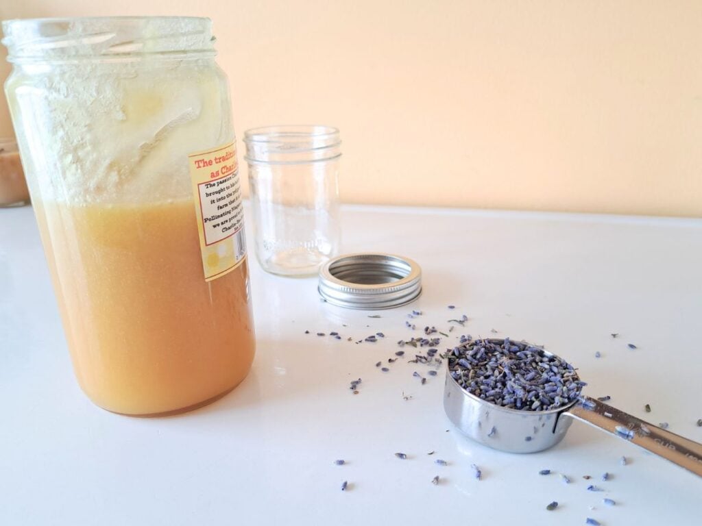 Dried lavender buds in a measuring cup with, a jar of honey, and a glass canning jar on the kitchen counter.