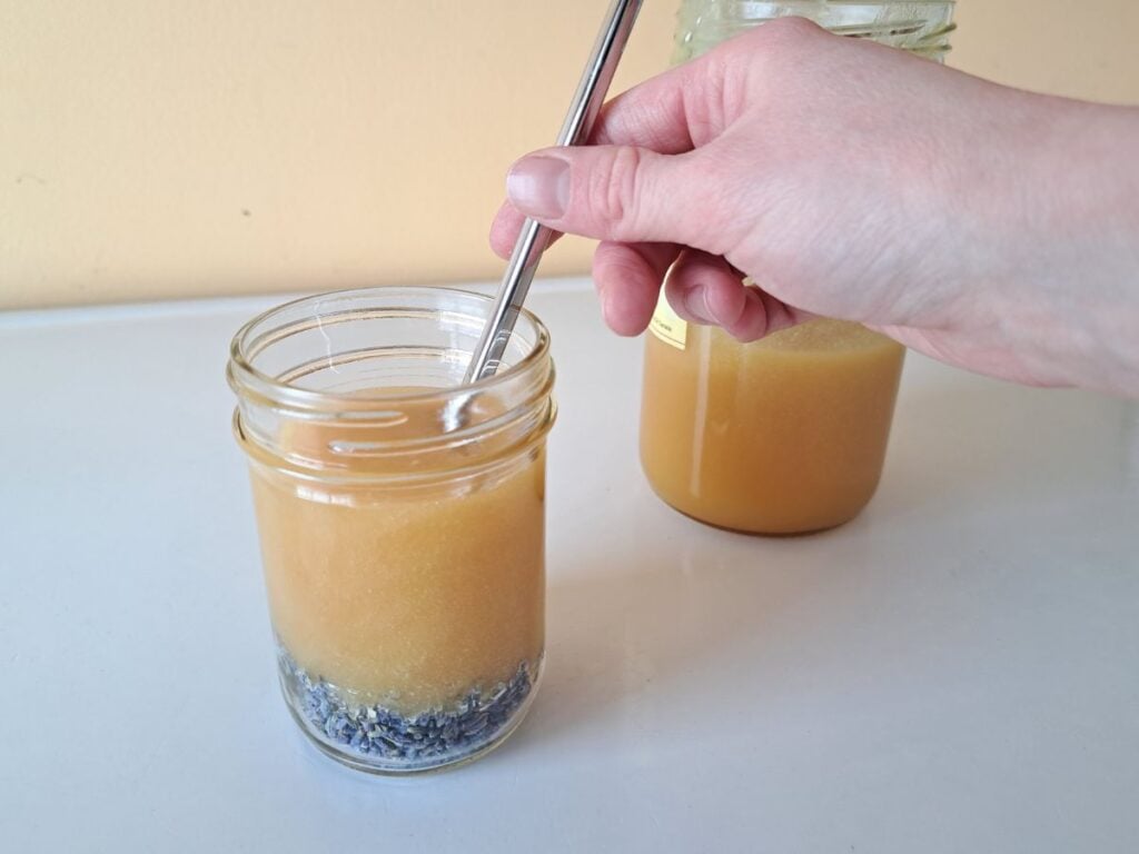 A hand using a chop stick to stir the honey and lavender together.