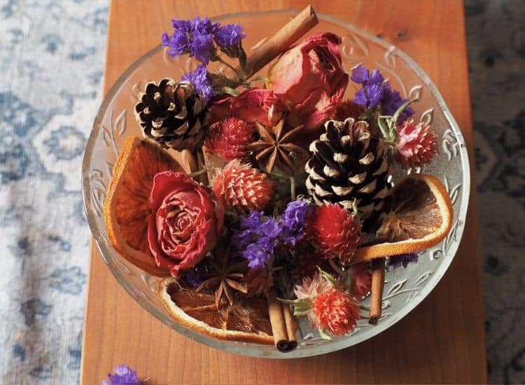 A collection of dried herbs, flowers, and pinecones in a potpourri bowl.