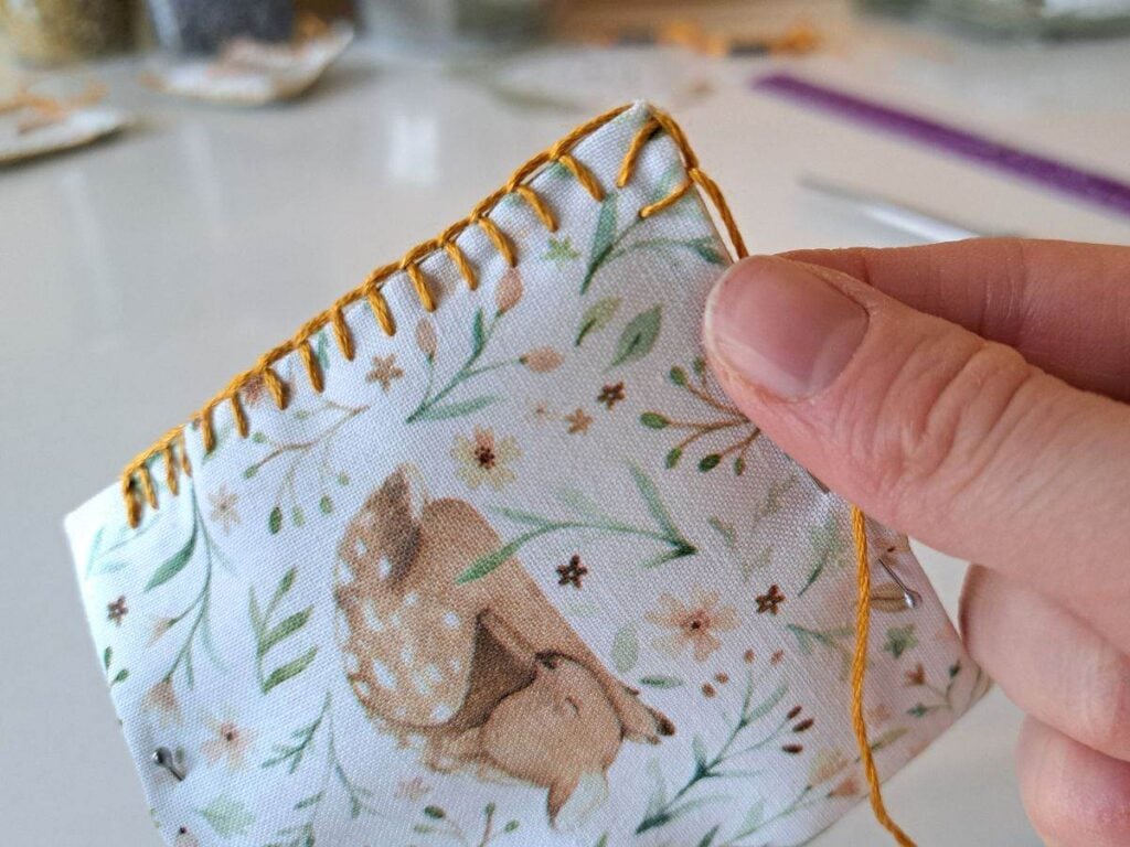 A hand holding an herbal sachet to show the detail of the blanket stitch on the corner.