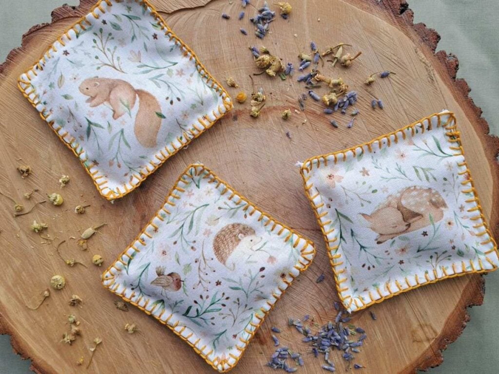 A close up of herbal sachets laying on a piece of wood with dried herbs around them.