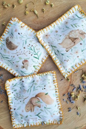Scented sachets laying on a piece of wood with dried herbs scattered around.