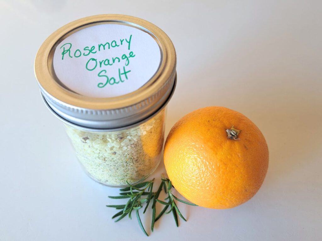 Rosemary orange salt in a glass canning jar with a sprig of rosemary and an orange sitting beside it.